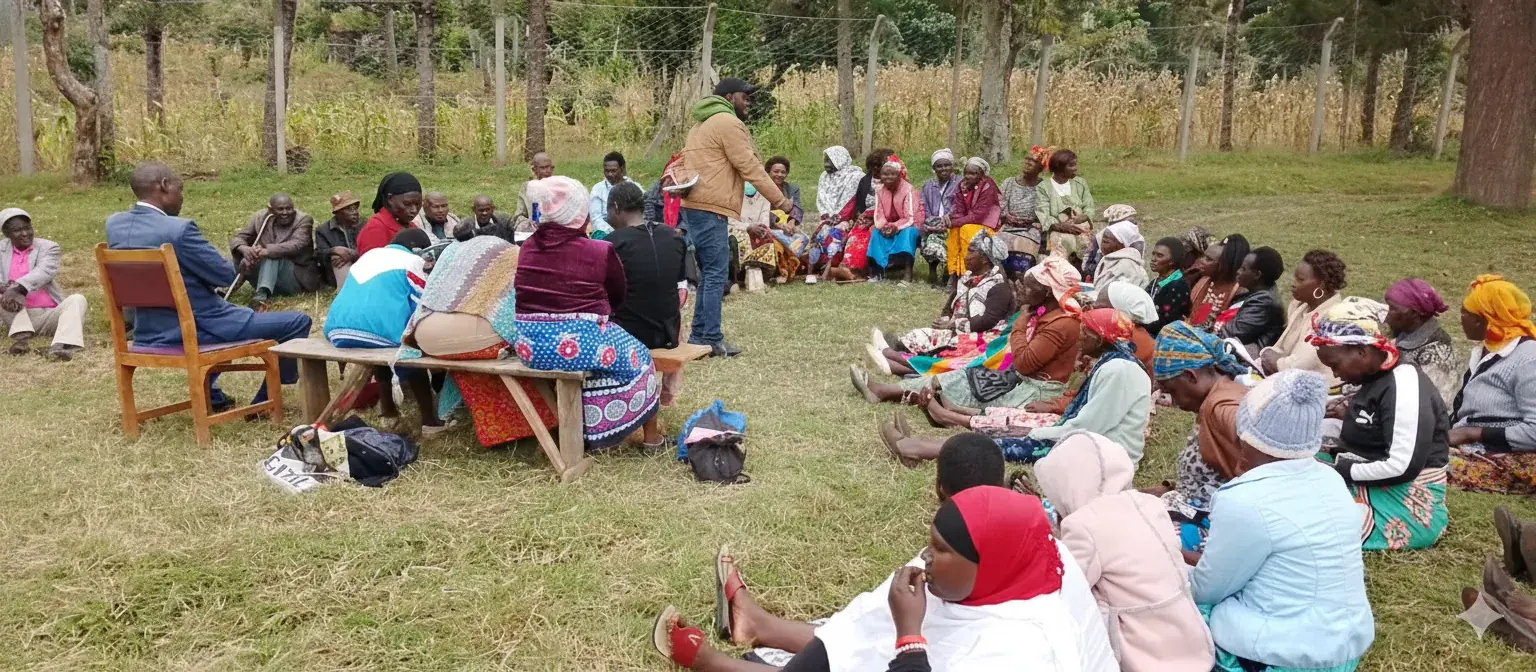 Community members seated in a field with a trainer